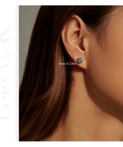 Detail of 6mm blue sapphire stud earring in gold claw setting worn on an ear