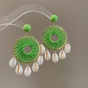 Détail de boucles d'oreilles créoles tissées avec fil vert et breloques en coquillage