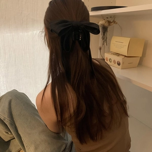 Detail of a large black satin bow hair claw clip worn on a woman's hair in warm lighting