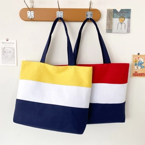 Detail of color-block canvas tote bags in yellow, red, and blue hanging on a wooden hook