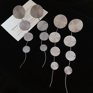 Macro view of silver tassel earrings with four textured metal discs on black velvet