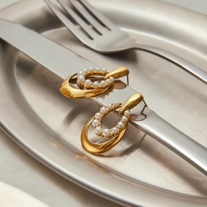 Macro shot of 18K gold-plated oval earrings with inlaid pearls on a silver cutlery backdrop