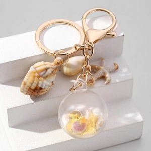 Detail van nautische sleutelhanger met zeester, schelpen en glitterbal op stenen decor