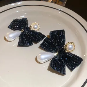 Elegant black bow earrings with large teardrop pearls and gold accent on a ceramic plate