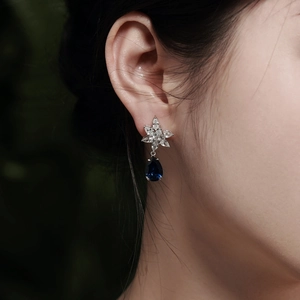 Detail of silver star earring with blue pear-cut gemstone worn by a model