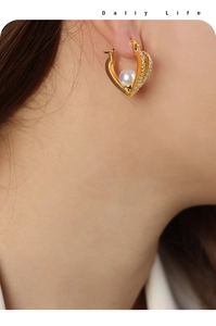 Close-up of elegant gold heart earrings with white pearl and sparkling crystals on model