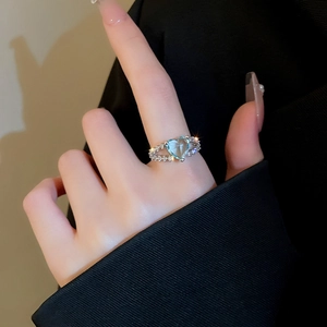 Detail of a double-layered silver ring featuring a heart-shaped light blue crystal on finger