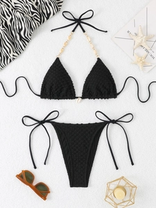 Close-up of black textured bikini set with shell details on white sand background