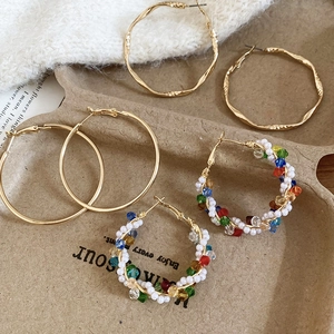 Detail of three metal hoop earrings with pearls and colorful beads on a textured tray