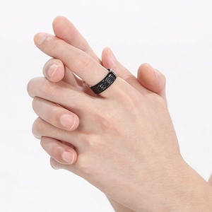 Detail view of a matte black titanium ring with triple grooved texture on a model's hand