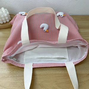 Detail of red striped canvas tote bag showing zipper closure and internal pocket
