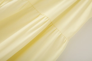 Detailed close-up of pale yellow layered fabric with delicate pleats and stitching