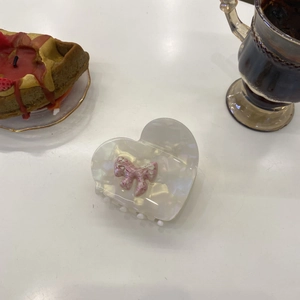 Detail of white marble acetate heart claw clip with pink bow in a lifestyle setting