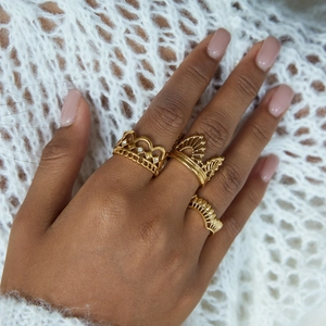 Detailed view of three gold crown rings with zircon lace patterns worn on a hand