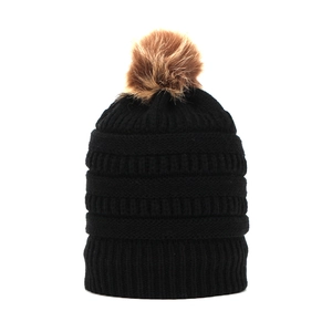 Close-up of black cable knit beanie texture with a soft brown faux fur pom-pom detail