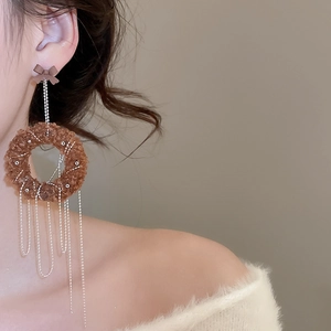 Detail shot of brown plush circle earrings with long silver fringe tassels on a model