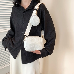 White heart-embossed crossbody bag with wide strap and circular coin purse pendant