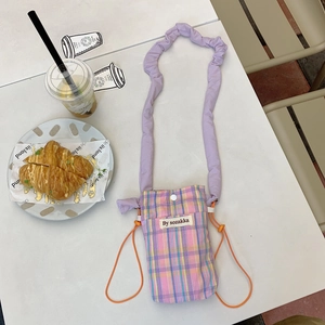 Detail shot of mini checkered crossbody bag with purple ruffled strap in a cafe setting