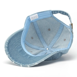 Detail of light blue denim baseball cap with distressed brim and 100% cotton tag