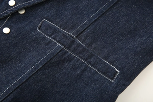 Detail of dark blue denim halter top featuring metallic buttons and side pockets with stitching