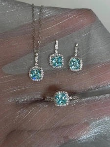 Close-up of light blue gemstone necklace, earrings, and ring set on silver mesh