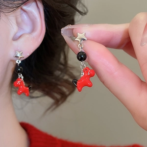 Detailed shot of silver star earrings with red pony pendants and black beads on ear lobe