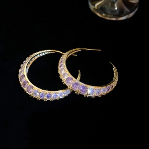 Detailed macro shot of gold-plated C-shaped earrings with purple zircon inlays