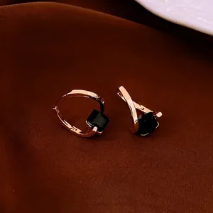 Rose gold hoop earrings with a square black gemstone on brown silk background