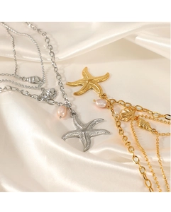 Close-up of gold and silver layered necklaces with starfish charms on white silk fabric