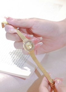 Detailed shot of a gold square watch with rhinestone bezel on a metal mesh band