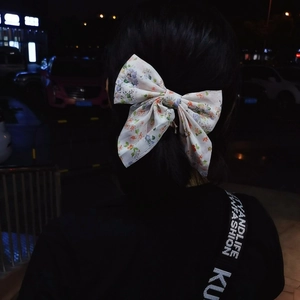 Floral bow hair clip worn on a ponytail, featuring purple and orange patterns on cream fabric