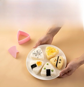 Pink triangular rice ball mold set with five decorated onigiri in a warm kitchen setting