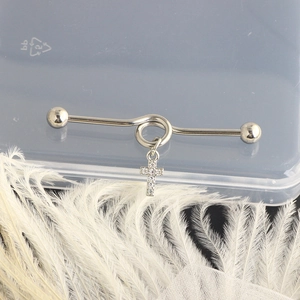 Silver industrial barbell piercing with cross pendant on soft white feathers