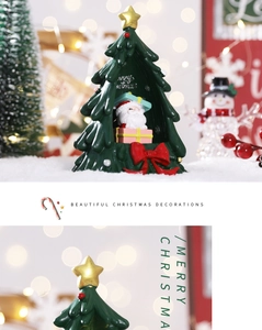 Detailed view of resin Santa in a green tree with golden star and red bow on snow