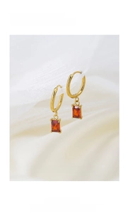 Detailed macro view of gold plated earrings with a red rectangular zircon stone