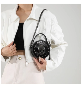 Detail of round black crossbody bag with silver skull stud and metal chain strap