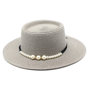 Dettaglio di cappello di paglia boater con nastro nero e accenti di perle bianche