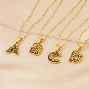 Detail view of 18k gold-plated A-D letter pendants on elegant silk fabric background