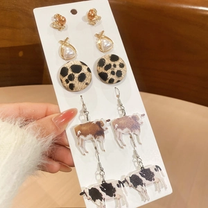 Close-up of pearl and cow print drop earrings on a white display card with winter styling