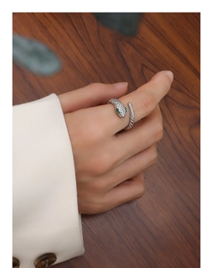 Macro shot of silver snake ring with green gemstone eyes on model's thumb