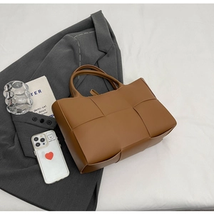 Flat lay of brown woven leather tote bag with gray blazer and aesthetic accessories
