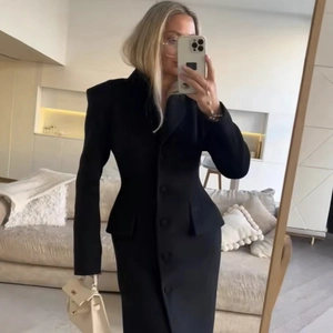 Women's elegant black wool coat with cinched waist and structured shoulders in a longline fit