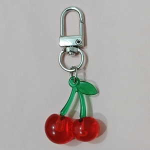 Detail of red cherry pendant with green leaves and silver metal spring clasp