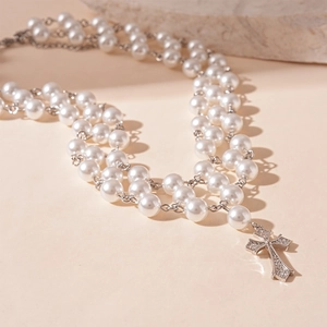 Détail du collier de perles à trois rangs avec un pendentif croix en argent et zircons