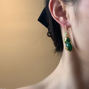 Detail view of vintage Chinese style gold gourd earrings with green gemstones on model