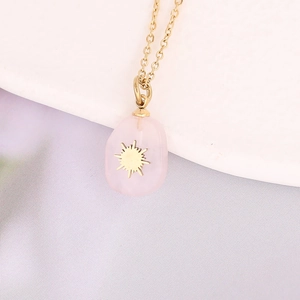 Detailed view of pink natural stone pendant with gold sun motif on a fine link chain