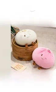 Close-up of soft plush steam bun pillows with cute embroidered faces in a bamboo steamer