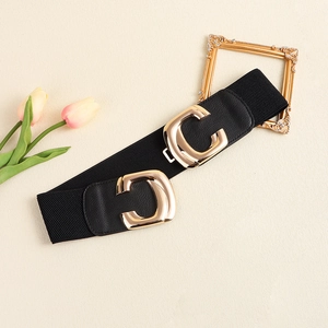 Detail of a wide elastic black belt with a gold C-shaped geometric metal buckle closure