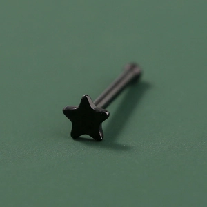 Macro shot of a black star-shaped stainless steel piercing stud on a green surface