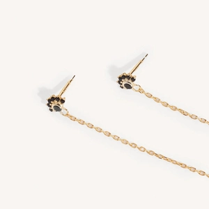 Golden eye flower earrings with black stones and long tassel chains on a white background